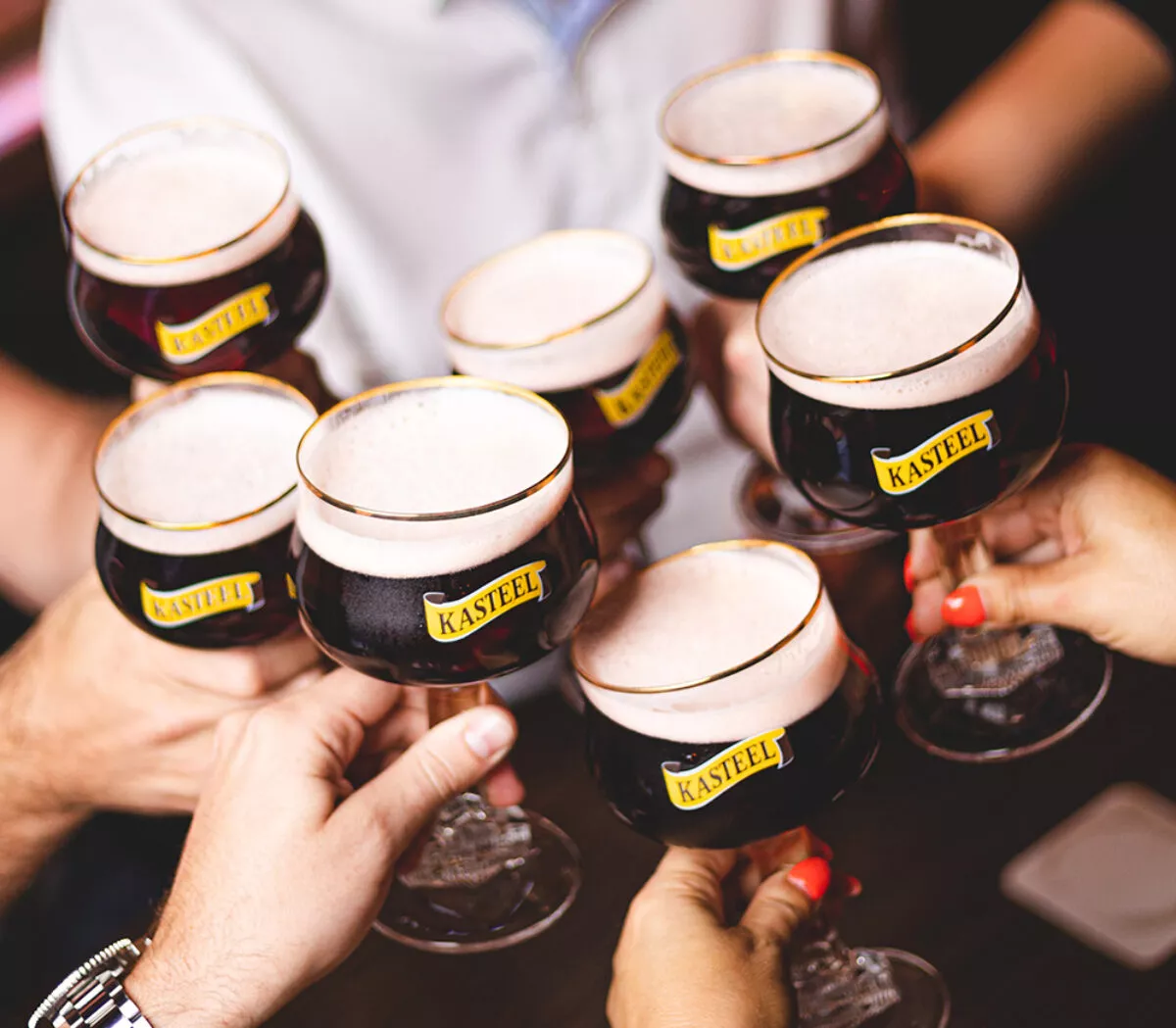 Zeven mensen klinken met een glas Kasteel Rouge, een sterk fruitbier gebrouwen door Kasteel Brouwerij Vanhonsebrouck.