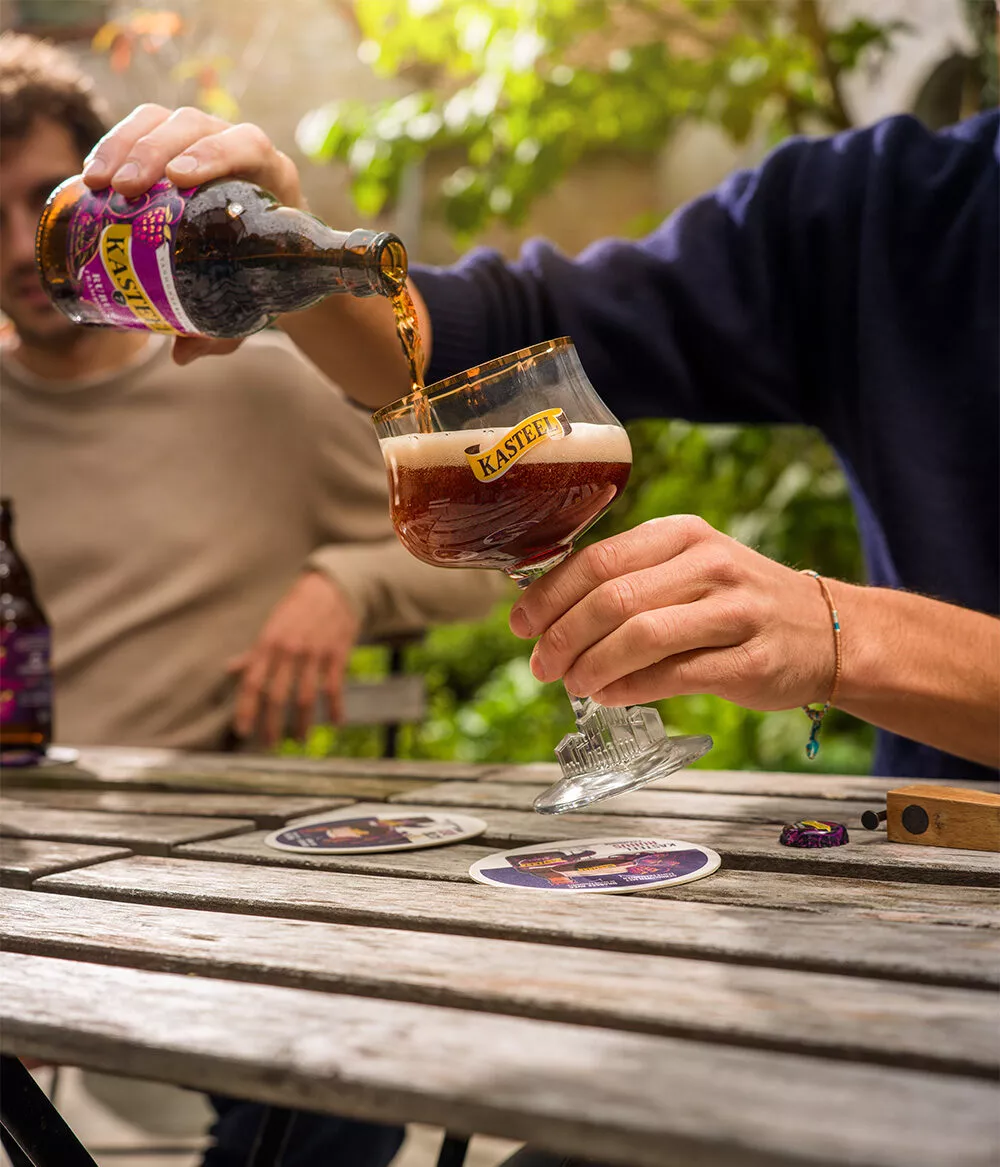 Een persoon schenkt een 33 cl fles Kasteel Rubus Framboise uit in een bierglas van het biermerk Kasteel. Het glas vult zich met een karmozijnrood bier met kleine schitteringen die door het bier razen en de lichtroze schuimkraag met gelijke bellen ondersteunen. Een sterk fruitbier gebrouwen door Kasteel Brouwerij Vanhonsebrouck.