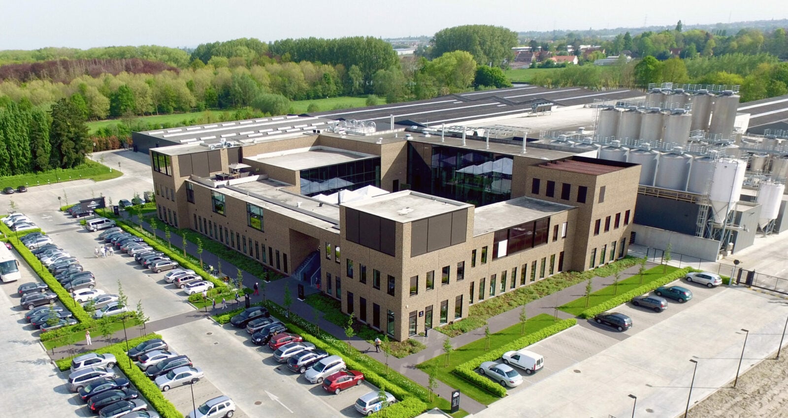 Luchtfoto van het Bierkasteel van Kasteel Brouwerij Vanhonsebrouck in Izegem, een moderne Belgische brouwerij met rondleidingen, evenementen en bierdegustaties, omgeven door groen en ruime parkeergelegenheid.